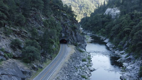 Aerial-following-car-on-canyon-road-entering-dark-tunnel-through-rocky-mountain