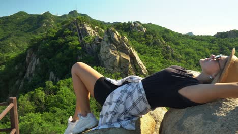 Female-Hiker-Relaxing-On-The-Rocks-At-The-Top-Of-Gwanaksan-Mountain-In-Seoul,-Lush-Mountain-Landscape-In-The-Background---trucking-shot