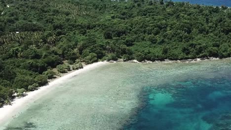 Flying-over-stunning-clear-island-beach-water-with-forest