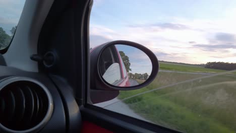 Traveling-by-car-on-the-highway-at-sunset,-through-the-rear-view-the-road-goes-backwards,-beautiful-landscape-in-the-background