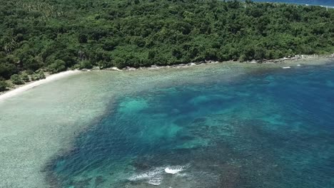 Drone-footage-over-blue-ocean-water-and-green-forest-inland
