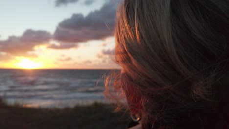 Woman-with-windswept-blond-hair-looking-at-sunset,-close-up,-slow-motion
