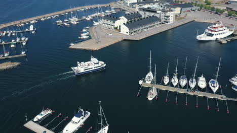 Aerial-drone-view-of-a-small-Scandinavian-city-port-with-a-passenger-vessel-transport-ship-boat-entering-the-harbor-at-the-end-of-a-trip-for-tourist-travelling-across-Swedish-sea-ocean-on-calm-waters