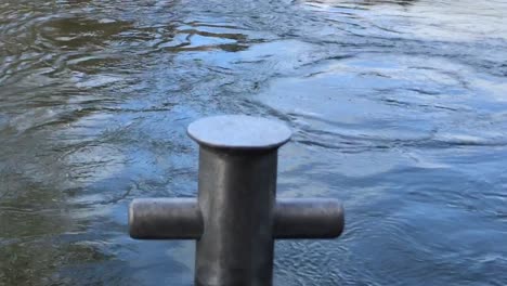 Close-up-of-the-Waikato-River-flowing-gently-passed-the-boat-anchor-capstan-on-a-bright-day-in-Hamilton-New-Zealand