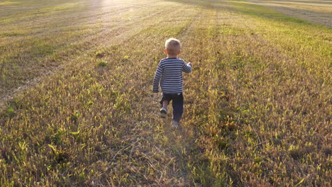 Young-boy-running-in-field-towards-golden-sunlight