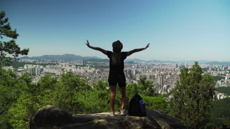 Sexy-Lady-Standing-On-The-Rock-Raises-Her-Hands-In-The-Air-At-Gwanaksan-Mountain-In-Seoul,-South-Korea