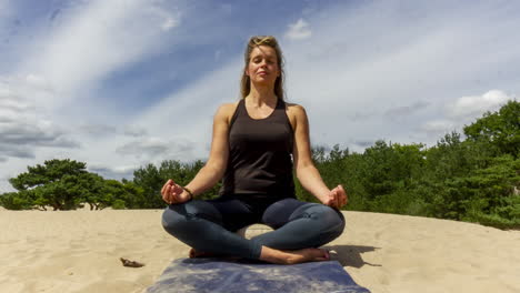 Time-lapse-of-Woman-sitting-still-in-lotus-pose-in-sand-dunes-with-clouds-forming-in-the-sky