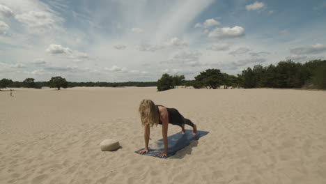 Woman-exercising-yoga,-doing-upward-facing-dog-in-sand-dunes-with-forest