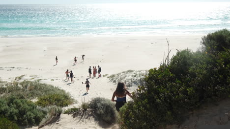 Rear-shot-of-pretty-young-girl-running-downhill-to-the-golden-beach,Australia