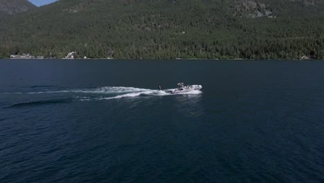Wakeboarder-and-tow-boat-with-mountains-in-the-background,-Montana---Aerial-Drone