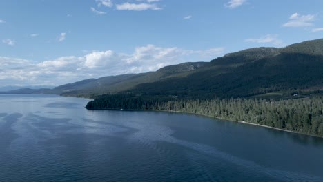 Atemberaubende-Landschaft-Des-Flathead-Lake-Mit-Dem-Immergrünen-Wald-An-Den-Bergen-In-Montana,-Usa-Unter-Dem-Strahlend-Blauen-Himmel