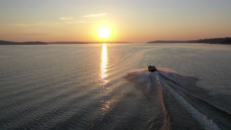 Boat-traveling-across-the-lake-heading-into-the-beautiful-golden-hour-sunset-from-a-aerial-view