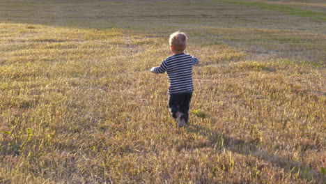 Toddler-boy-runs-through-harvested-field,-slow-motion-shot