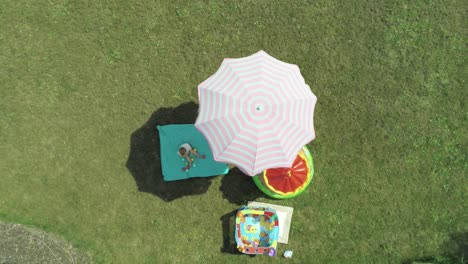 Langsam-über-Einem-Kleinen-Kind-Absteigend,-Das-An-Einem-Heißen-Sonnigen-Tag-Im-Schatten-Eines-Regenschirms-Spielt,-Antenne