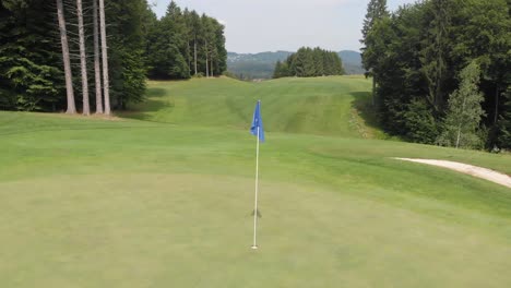 Blaue-Flagge-In-Einem-Golfloch-Auf-Einem-Wunderschönen-Golfplatz-Mitten-Im-Wald