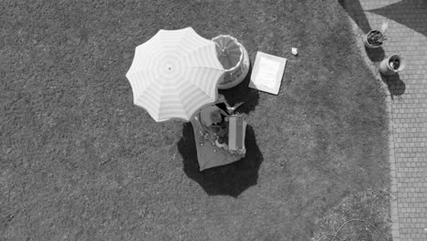 Slowly-ascending-above-a-mother-and-child-sitting-in-the-shade-of-an-umbrella,-aerial-black-and-white