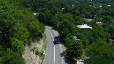 A-Black-SUV-Driving-Alone-On-The-Asphalt-Road-In-The-Mountain-With-Lush-Trees-In-Racha,-Georgia-On-A-Fine-Weather---aerial