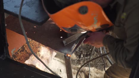 Man-Welding-a-Piece-of-Metal-Wearing-a-Mask-for-Light-Protection,-Slowmo