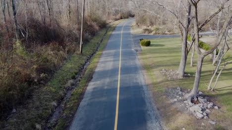 drone-flying-along-a-road-with-a-yellow-line-you-can-also-see-trees-without-leaves-and-a-small-water-gully
