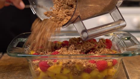 Adding-the-crumble-to-a-peach-raspberry-crisp---isolated-close-up