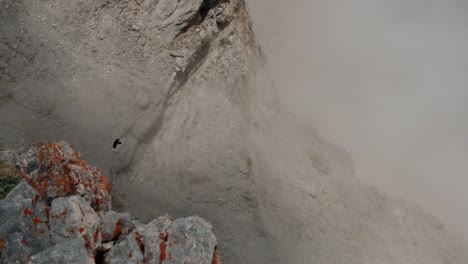 A-Crow-Flying-In-High-Altitude-Through-The-Rocky-Mountains-On-A-Foggy-Day---high-angle-slowmo-shot