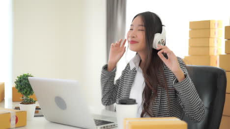A-young-woman-sitting-at-her-office-desk-working-on-her-laptop-and-listening-to-music-through-her-headphone-dances-to-the-tunes