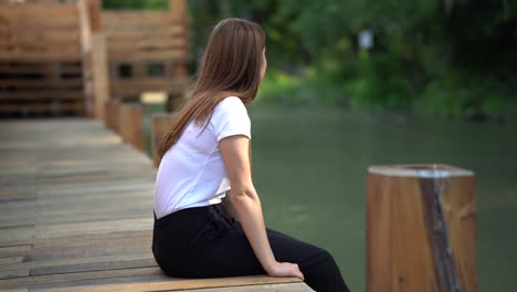 Young-caucasian-girl-sitting-on-side-of-wooden-bridge-looking-into-distance