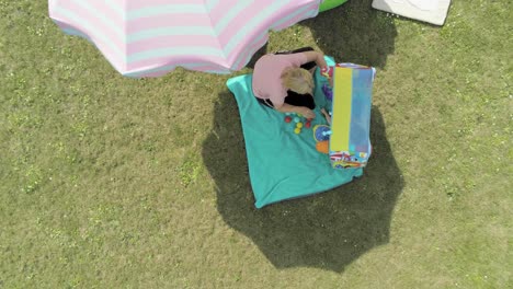 Looking-down-on-a-mother-playing-with-her-child-under-an-umbrella-in-the-backyard,-aerial