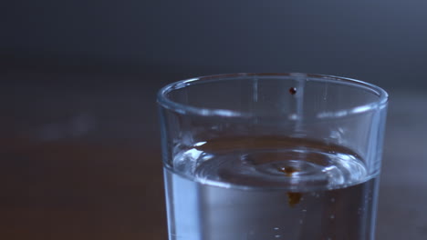 Dark-colored-liquid-drops-into-a-glass-of-water-and-spreads