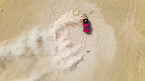 Drone-looking-down-on-a-red-truck-doing-doughnuts-in-the-desert,-kicking-up-big-clouds-of-sand-dust
