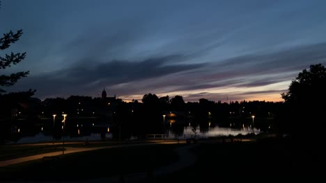 Darkening-timelapse-of-blue-hour-sunset-over-urban-park-lake-reflection-with-path