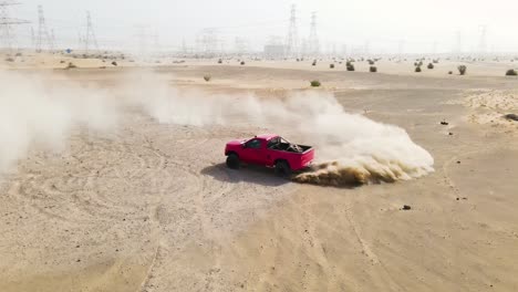Slow-motion-drone-view-of-a-red-truck-spinning-tires-doing-a-doughnut-kicking-up-a-dust-cloud-in-a-sandy-desert-area