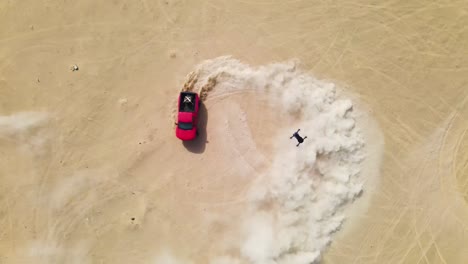 Drohne,-Die-Auf-Einen-Roten-Lastwagen-Herabblickt,-Der-In-Der-Wüste-Hochgeschwindigkeits-Donuts-Macht-Und-Große-Wolken-Aus-Sandstaub-Aufwirbelt