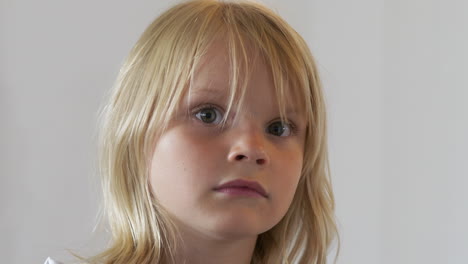 Handheld-Close-portrait-of-young-blonde-girl-on-white-background,-kind-face-turns-serious-in-slow-motion