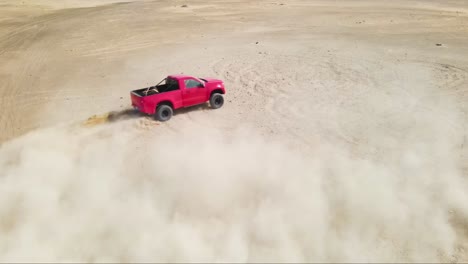 Slow-motion-shot-of-a-red-truck-sliding-and-spinning-its-tires-off-road-in-a-sandy-desert