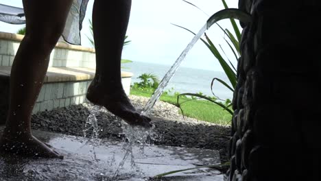 Slow-motion-woman-washing-feet-with-water-after-visiting-beach-palm-trees-and-pool-in-background
