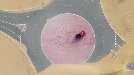 Top-down-drone-view-of-a-red-truck-drifting-on-a-roundabout-in-the-middle-of-the-desert