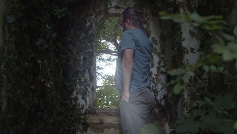 Man-stares-through-ivy-covered-ancient-church-window,-slow-push