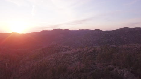 Drone-view-of-the-sun-setting-over-the-sparse-pine-tree-filled-landscape-of-the-Delamar-Mountains-in-the-San-Bernadino-Forest-in-California