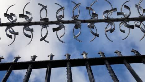 Prison-barbed-wire-steel-gate-looking-up-to-blue-cloudy-sky-slow-right-dolly