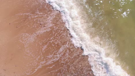 Top-aerial-view-of-stunning-tropical-vacation-beach,-waves-crashing-against-pink-shore,-spiral-down