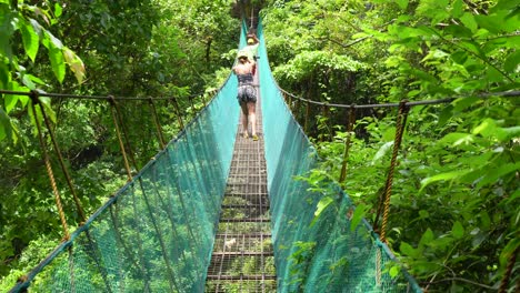 Lovely-Asian-Woman-Following-The-Tourist-Guide-While-Walking-On-A-Hanging-Bridge-In-The-Middle-Of-Lush-Green-Forest-In-El-Nido,-Palawan,-Philippines---Medium-Shot