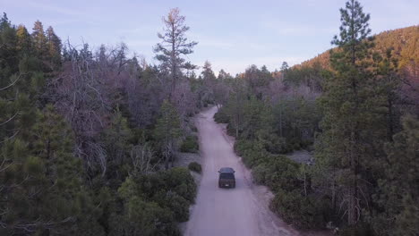 4WD-vehicle-driving-through-forest-mountain-road,-rising-aerial-reveal