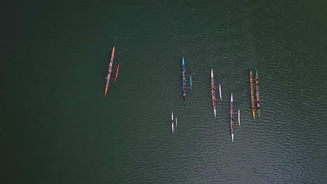 Aerial-top-down-view-above-colourful-teams-of-athletes-in-long-rowing-boats-on-lake