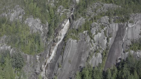 Quiet-breathtaking-stunning-aerial-hold-close-up-of-the-mountain-side-of-icy-rushing-waterfalls-coming-down-ythe-cliff-covered-trees-of-Shannon-Falls-BC-Squamish-in-the-summer