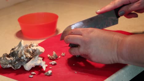 Hands-breaking-up-a-cluster-of-maitake-mushrooms,-then-slicing-on-a-red-cutting-board-with-a-santoku-chef-knife-and-finally-putting-cut-mushrooms-into-a-bowl