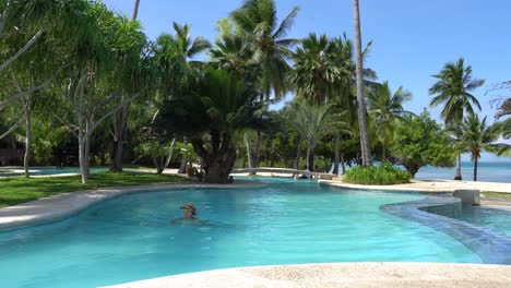 Niña-Nadando-En-La-Piscina-En-Un-Día-Soleado-Con-Exuberantes-árboles-Verdes-En-Dos-Palmas-Island-Resort-And-Spa,-Puerto-Princesa,-Palawan,-Filipinas