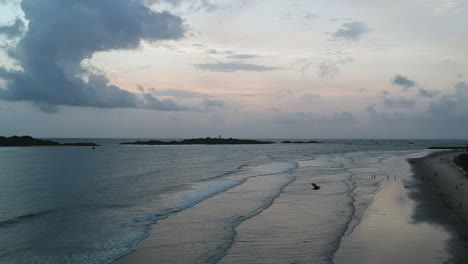 Luftaufnahme-Von-Strandwellen-Mit-Felsen-In-Der-Ferne-Und-Krähen,-Die-über-Den-Rahmen-Fliegen,-In-Mangalore,-Indien,-Abenddrohnenaufnahme