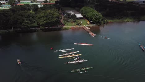 Aerial-descending-view-towards-colourful-group-of-long-athletes-row-boats-on-lake-water