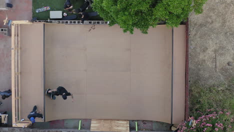 Skaters-on-homemade-mini-ramp-in-backyard,-aerial-top-down-view